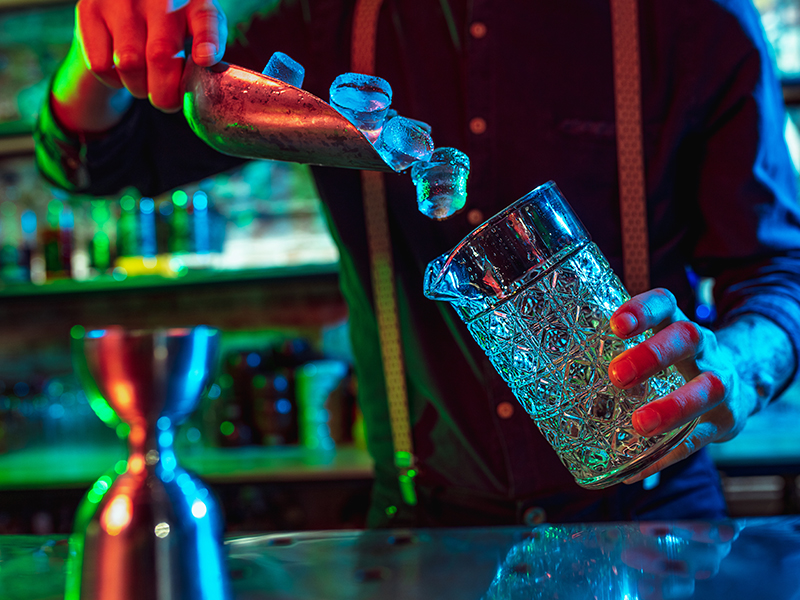 Nightlife Close up of barman finishes preparation of alcoholic cocktail in multicolored neon light
