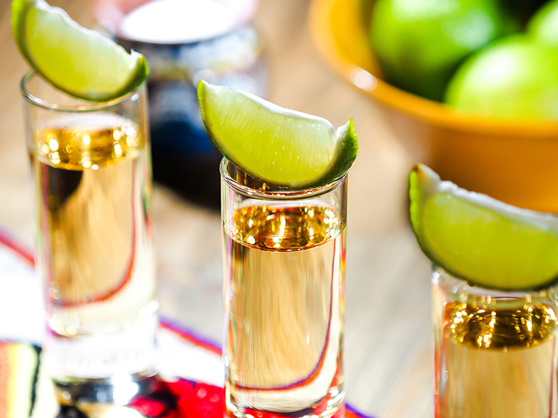 tquila Three shots of tequila in tall shot glasses with lime wedges on top